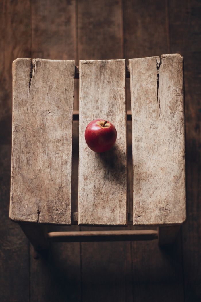 social-feed-img-01 Top view of a red apple on a rustic wooden stool, capturing an autumn aesthetic.