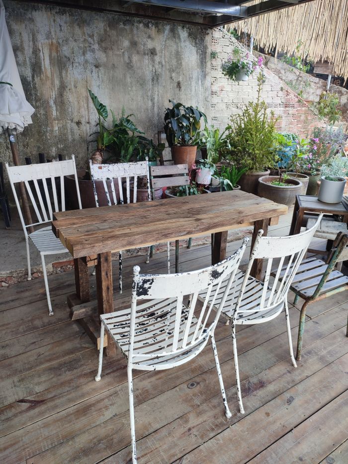 Cozy outdoor patio with rustic chairs and table surrounded by lush potted plants.