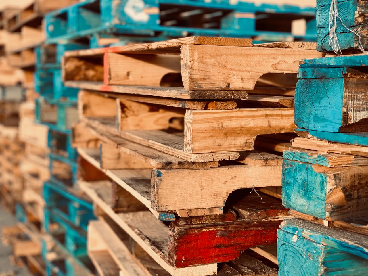 social-feed-img-03 Close-up of colorful stacked wooden pallets in outdoor sunlight.