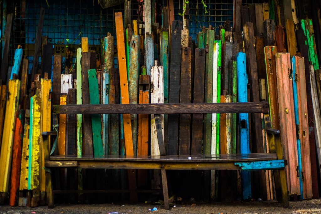 A vibrant arrangement of colorful wooden planks behind a rustic wooden bench, providing an urban art vibe.