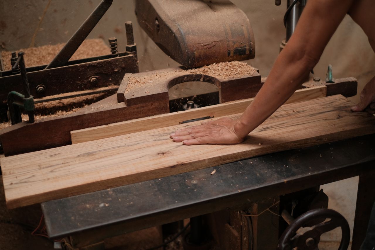 A carpenter skillfully operating a wood planer, shaping a wooden board in a workshop setting.
